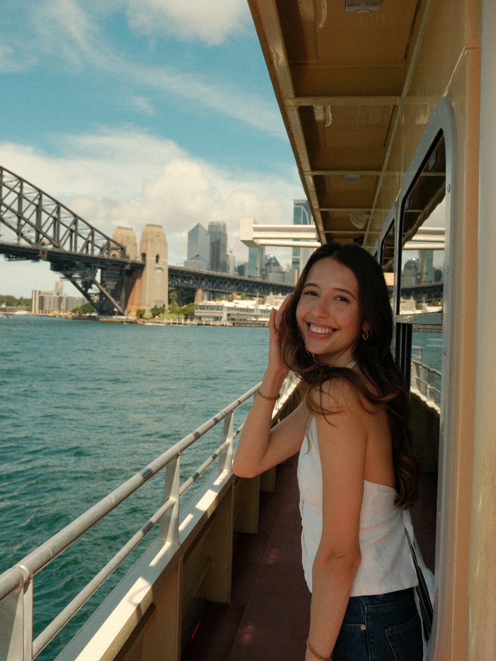 Luiza smiling on a Sydney ferry with the Harbour Bridge behind